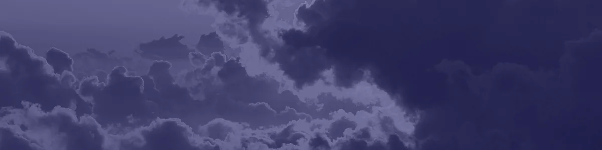 Tinted detail of a photo: Tops of billowing clouds seen from above at sunset, dark grey masses edged with glowing gold where the sun shines through, under an orange sky.