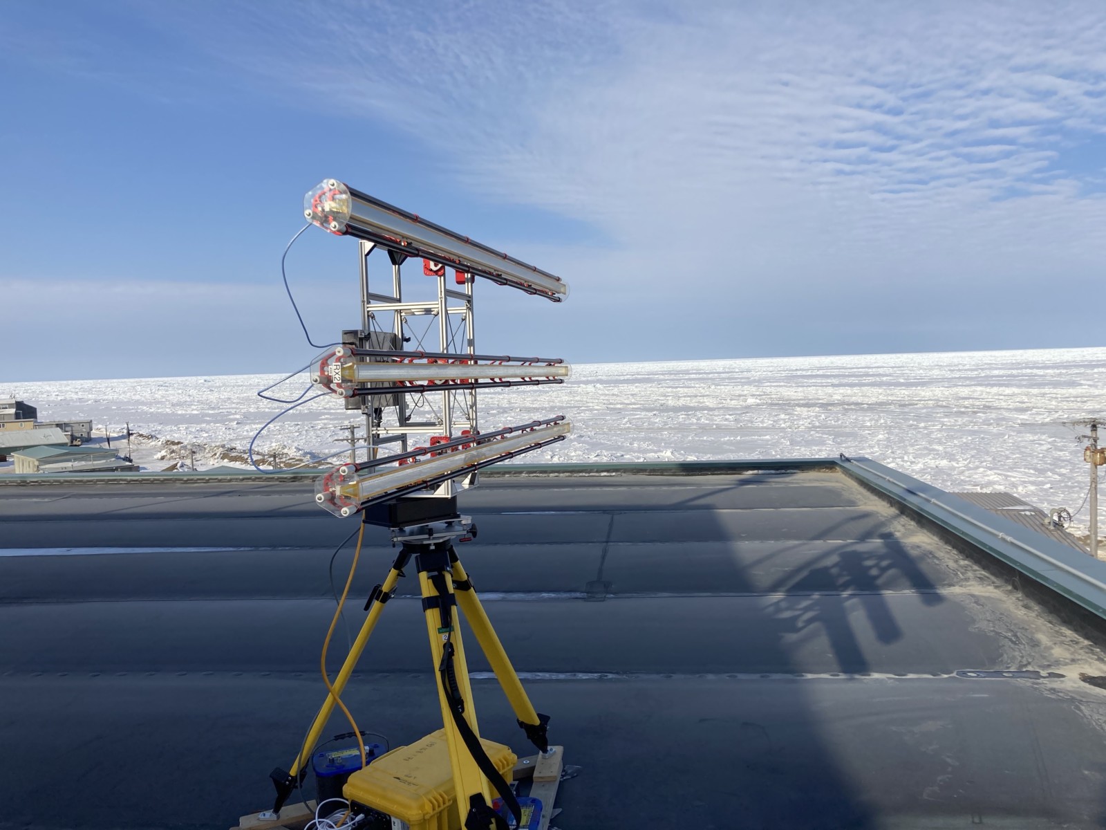 An instrument stands directed at the wide ice covered horizon with blue skies in the background.
