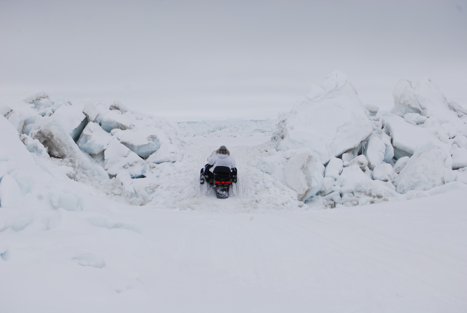 Person on snow machine drives up icy slope in wide ice landscape
