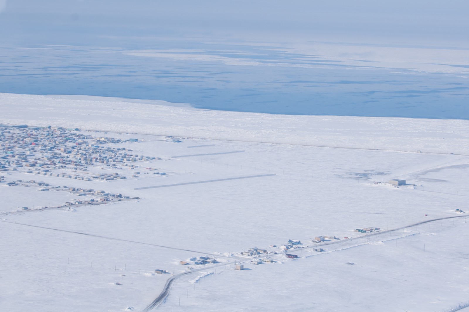 Airborn view on a wide snow landscape with a settlement and airstrip.