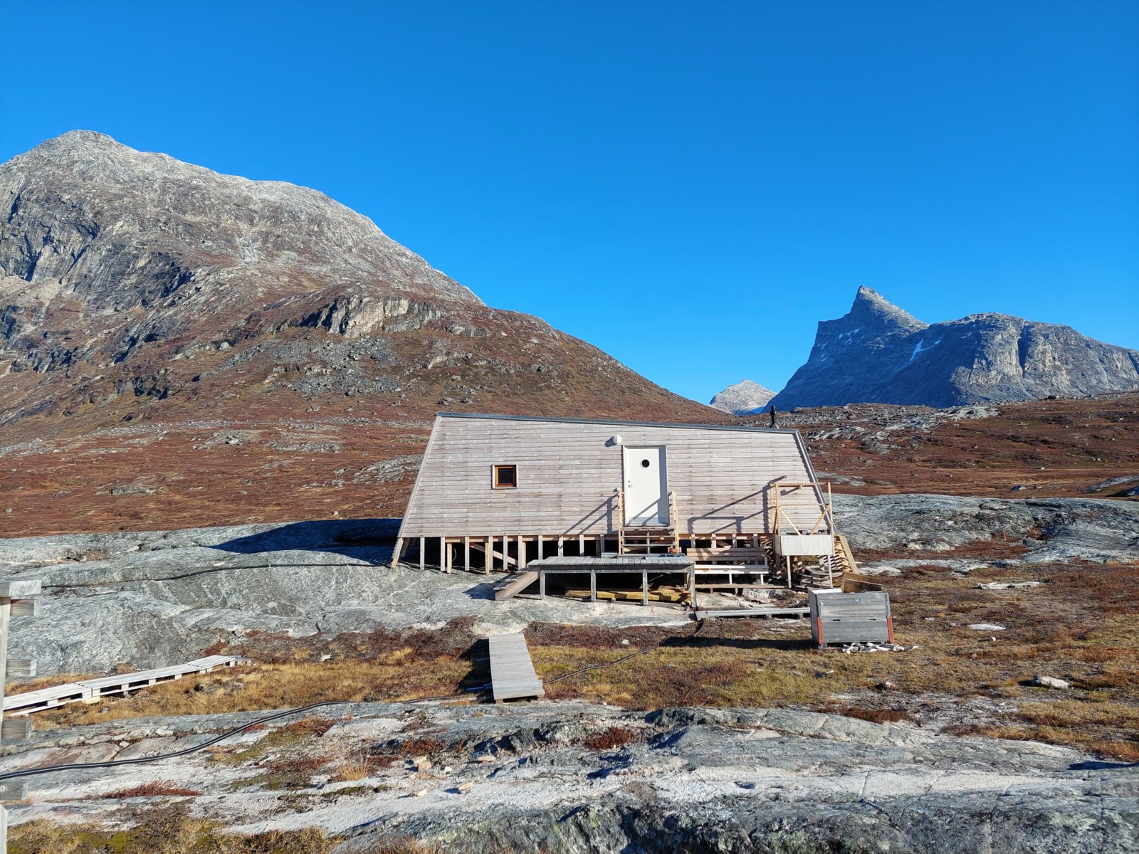 The wooden Kobbefjord research station before bright blue skies and mountains in the background.