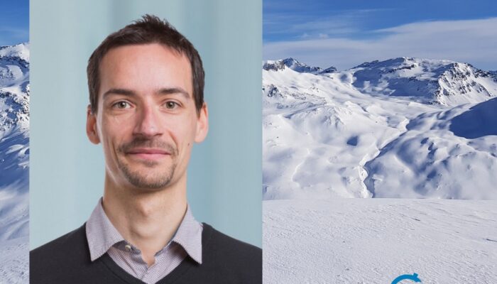 A profile image of a white man with beard, shirt and pullover in front of a glacier landscape.