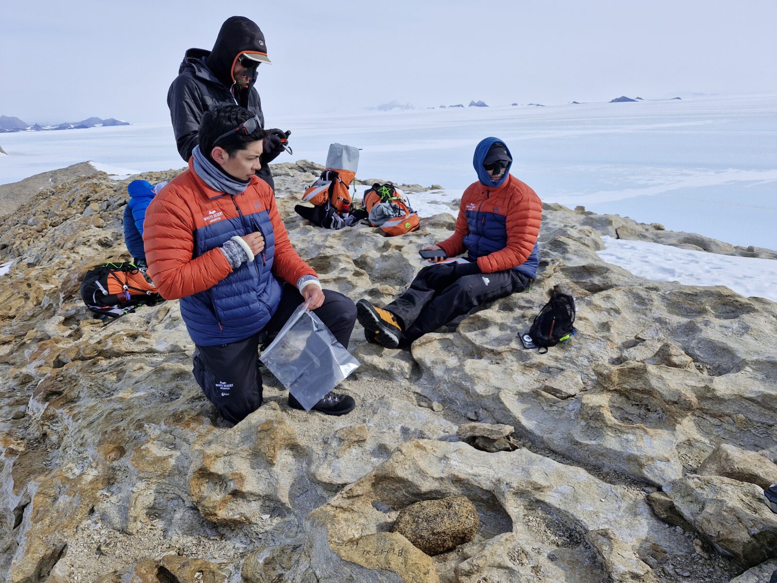 Scientists sat on a rock in Antarctica collecting rock samples.