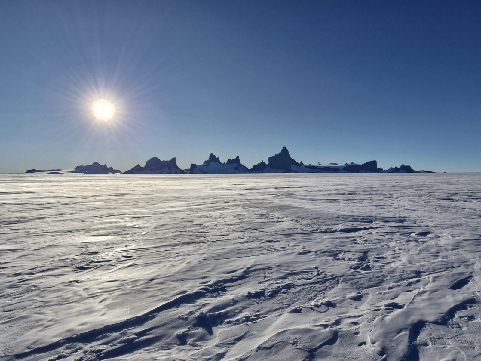 Ulvetanna Peak and surrounding rocky outcrops on the background of deep, clear blue sky. Taken in late December 2024, when the sun remains above the horizon in Antarctica.