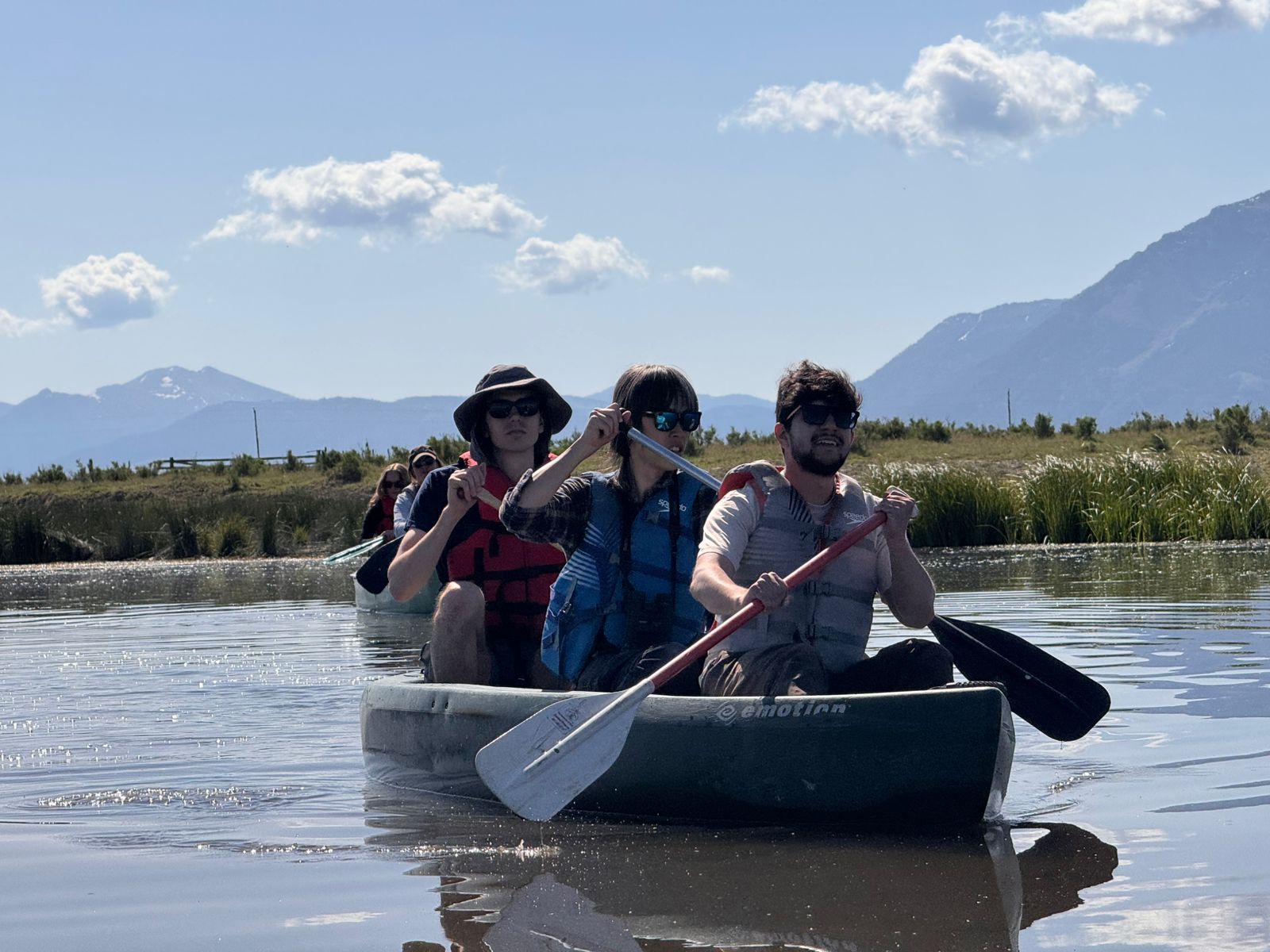 A group of three individuals in a canoe on a lake, with mountain in the distance.