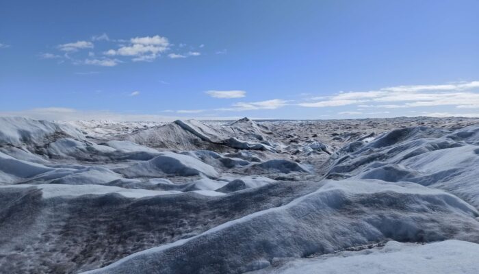 Below a clear blue sky, ridges of ice undulate towards the horizon in stripes of white, blue, and black.