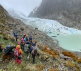 a group of students and staff in hi-vis rain gear pick theri way along a rocky slope towards a glacier