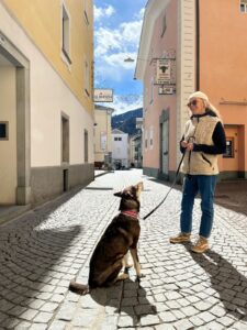 The researcher stands between buildings on a cobblestone path with a dog on a leash