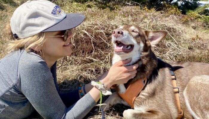 a scientist lays on the grass with a dog in the sun. Its a casual setting with camping equipment scattered around them
