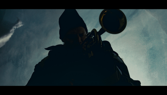 against a blue, muted sky a saxophone layer in a beanie plays a song