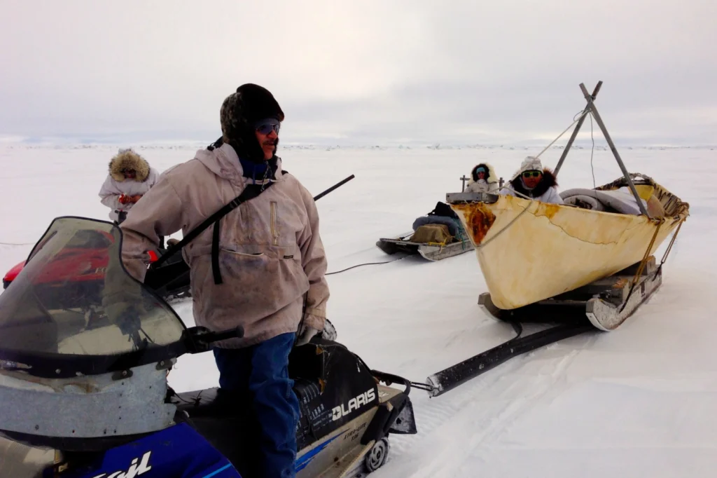 Man on snow machine looks bake to the canoe he is towing across ice.