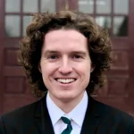 Person with curly hair, smile and black and white suit and tie.