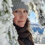 Woman with knitted hat peaking though snow-covered trees.