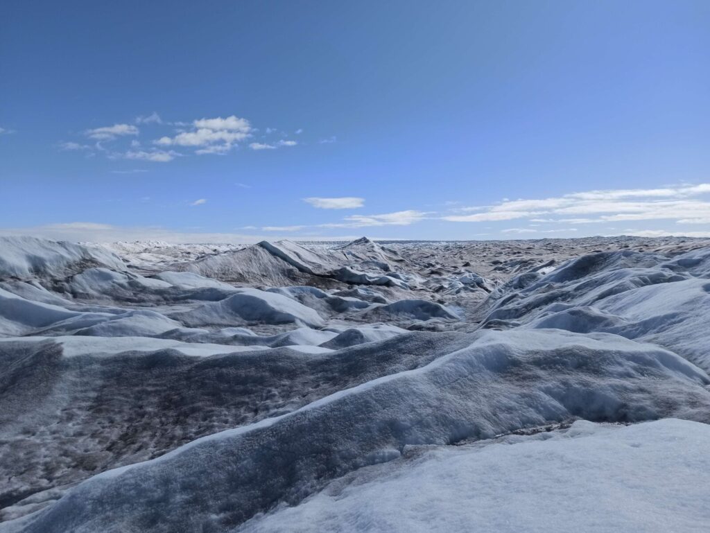 Below a clear blue sky, ridges of ice undulate towards the horizon in stripes of white, blue, and black.