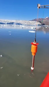 Bright orange intrument is suspended over an icy ocean