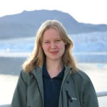 Young scientist stands in front of glacier under a blue sky