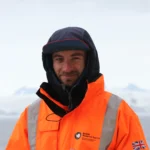 Man in orange coat in front of glacier