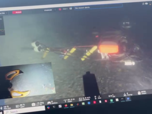 A view from the remote vehicle. It is a dark and somewhat blurred image of a claw about to grab an item from the ocean floor