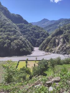 A narrow river valley between two relatively steep hills which are covered in vegetation. 