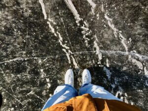 a photo orientated downwards, showing legs standing, with ice skates on, on ice. 