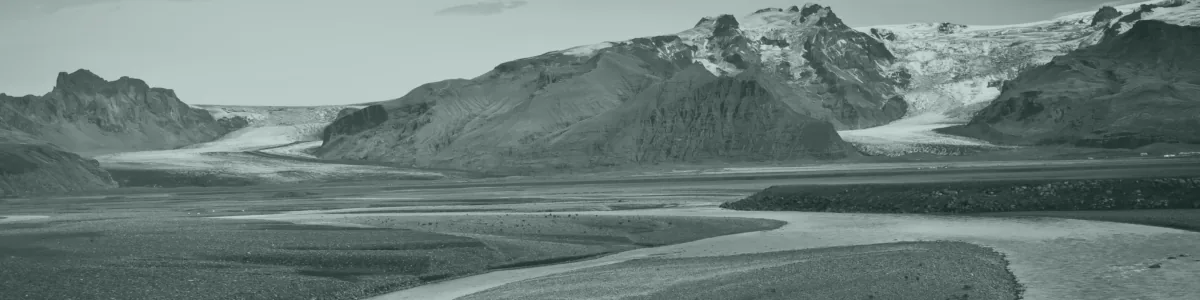 Tinted detail of a photo: Broad grey gravel outwash plain crossed by shallow braided channels of muddy water, with two glacier tongues flowing between dark mountains under a cloudy sky.