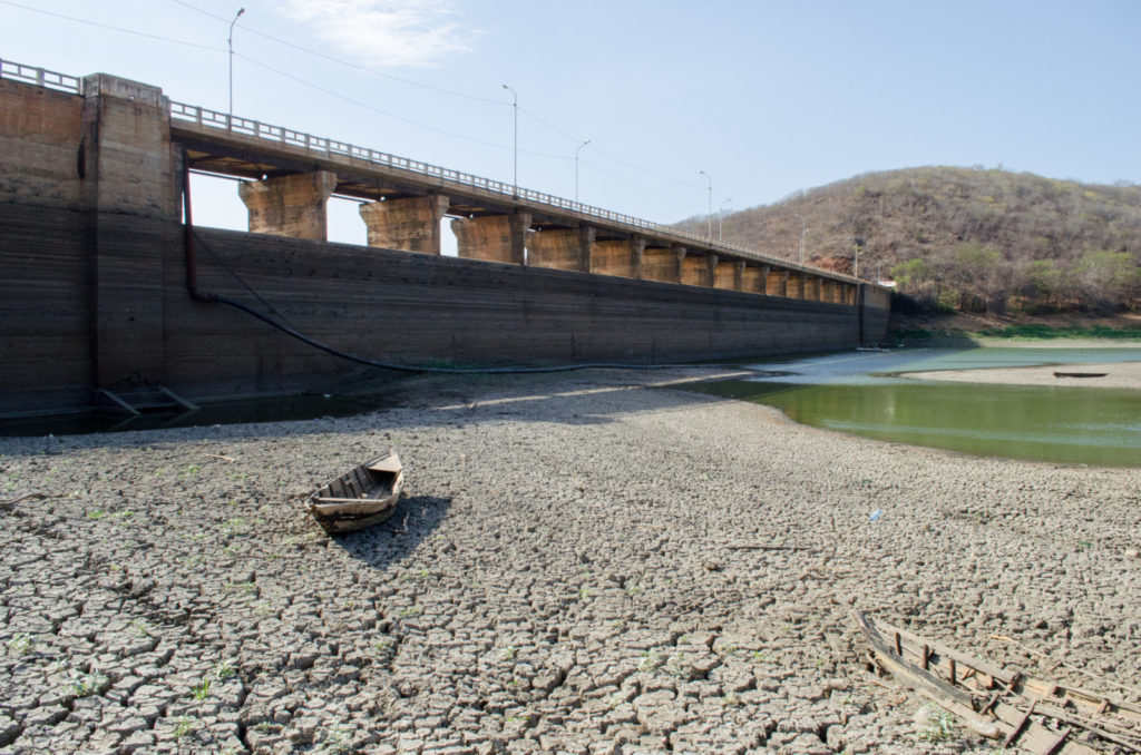A dam, an almost empty water reservoir and a small abandoned boat