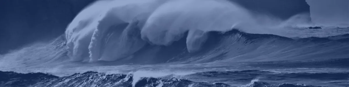 Tinted detail of a photo: Huge breaking wave with spray streaming back from its crest in front of dark cliffs topped by a house and telegraph poles, under a gloomy sky.