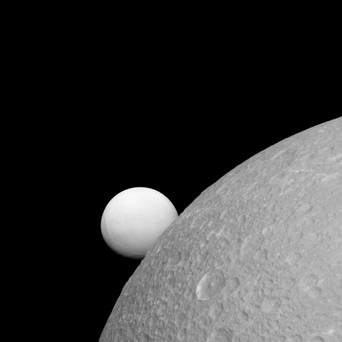 Although Dione (near) and Enceladus (far) are composed of nearly the same materials, Enceladus’ surface is much brighter. Credit: NASA/JPL-Caltech/Space Science Institute.