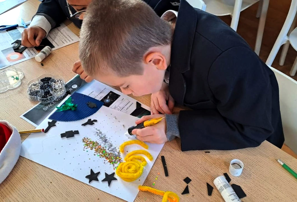 Young student at the Bogaert School attempts to create a tactile image reresenting space weather, learning about the challenges blind and visually impaired students face. The student in a black jacket is creating an image with yellow pipe cleaners, glue and cut out sections of different textured paper.