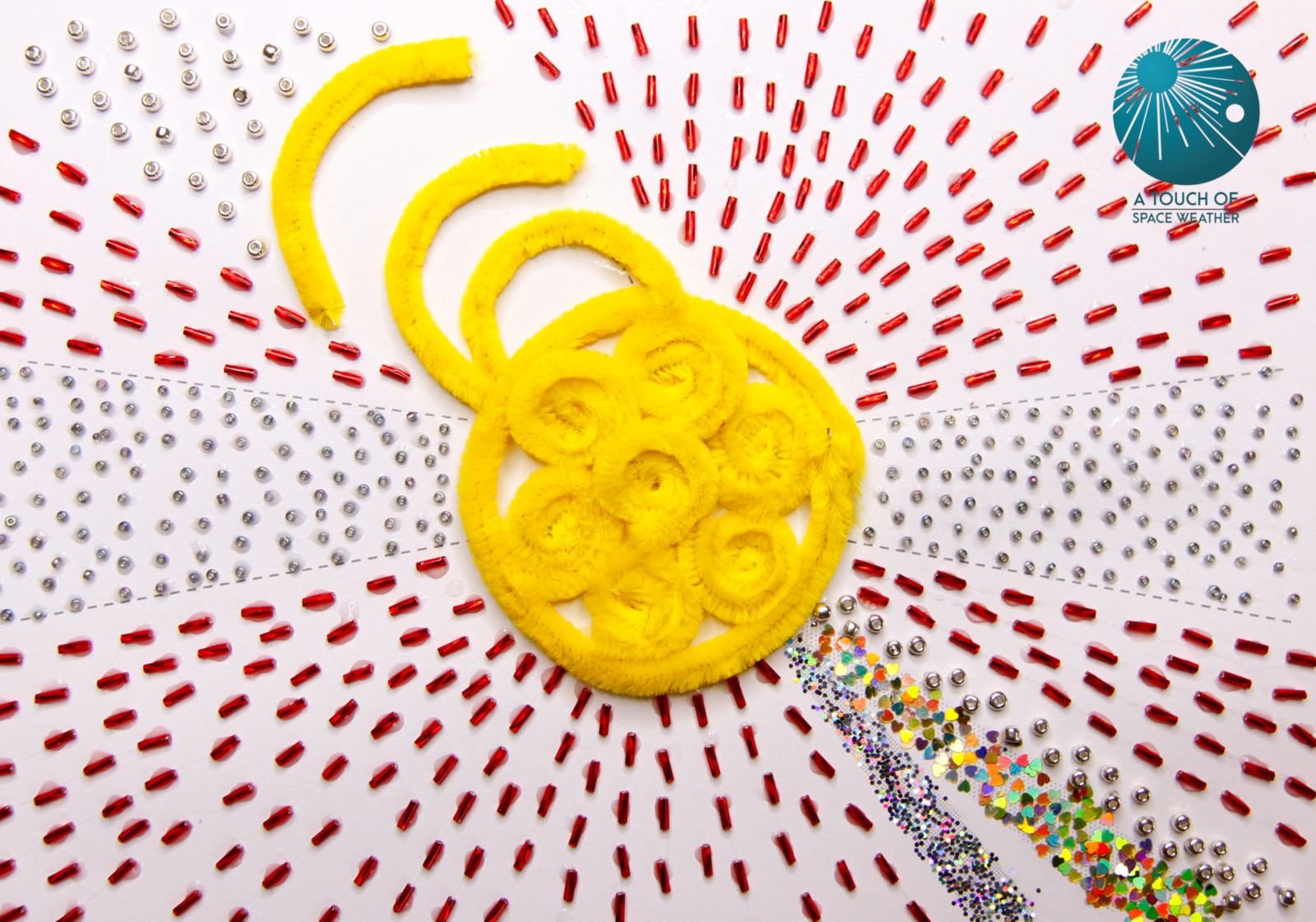 Looping yellow pipe cleaners curled togetehr in the centre surrounded by rays of red, black and multicoulred beads of various sizes, radiating outwards from the yellow sun in the center.
