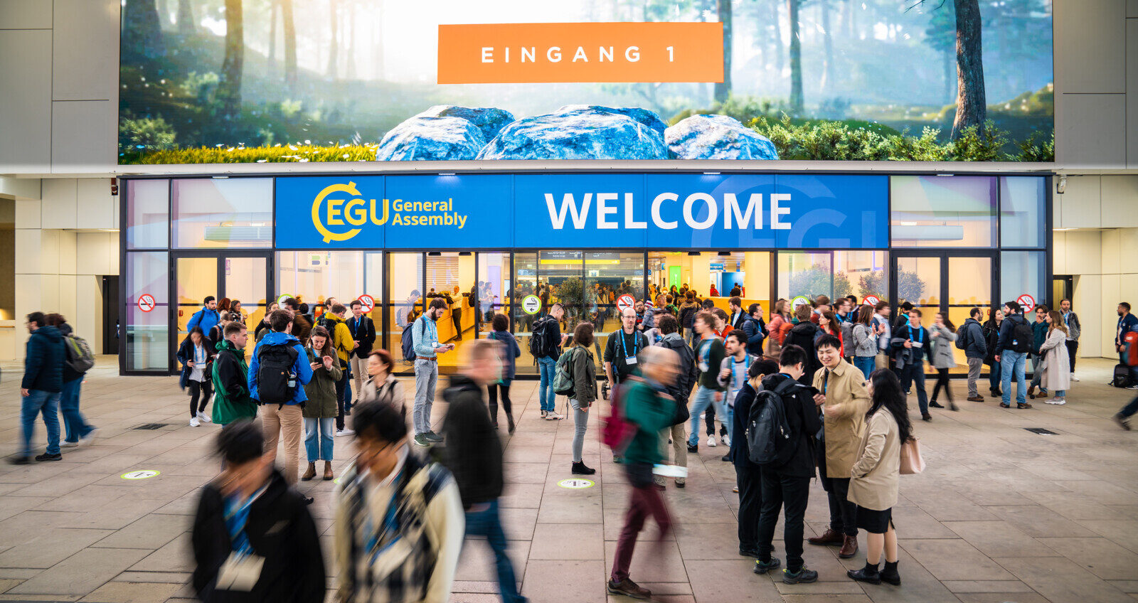 conference participants standing outside of building entrance, with blue sign EGU: Welcome
