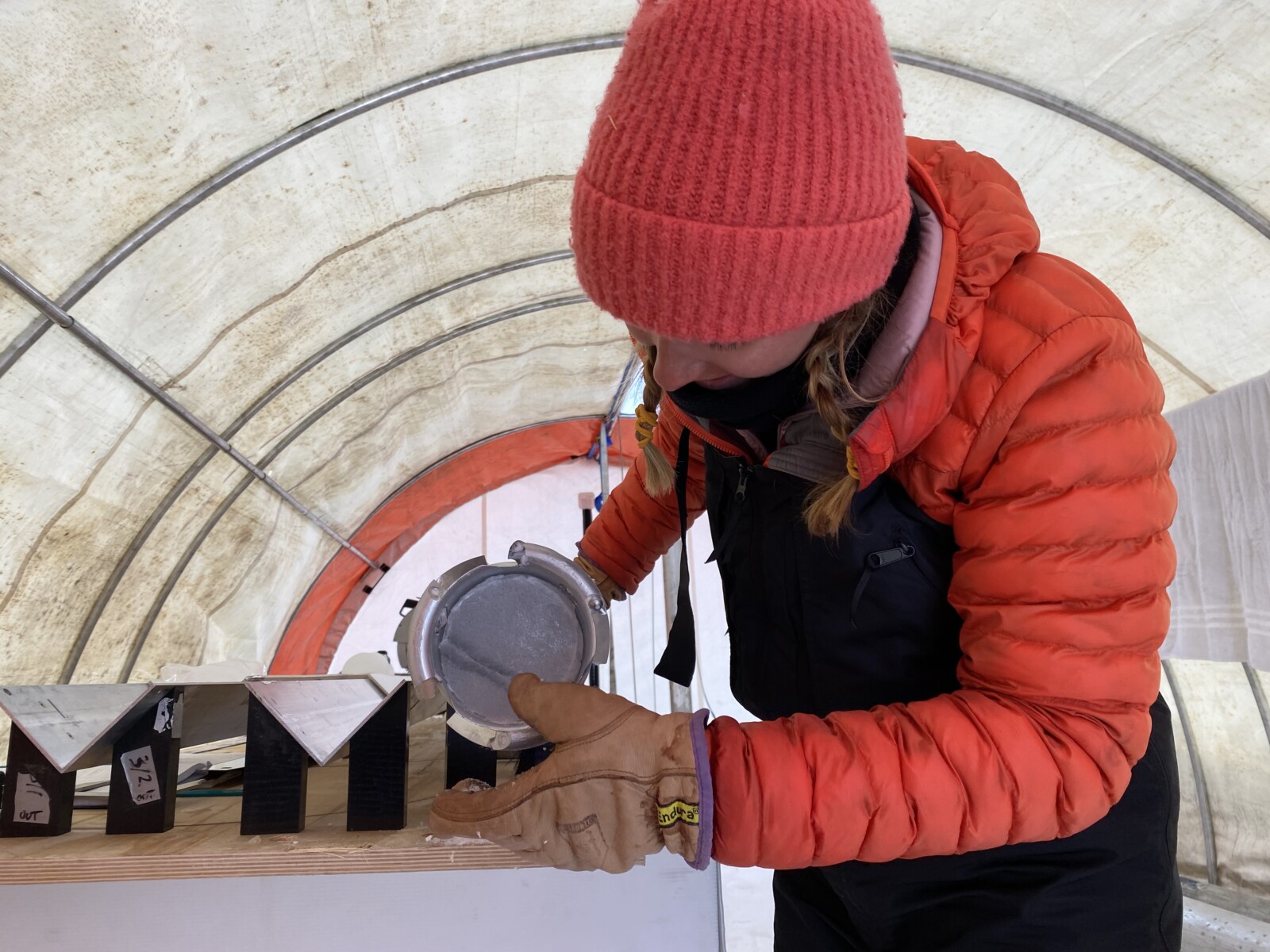 Emma, in an orange puffer jacket, looks at the cut of a freshly taken ice core