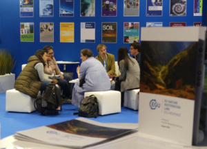 The image shows researchers networking and chatting about Science Policy at the EGU booth in 2023. 