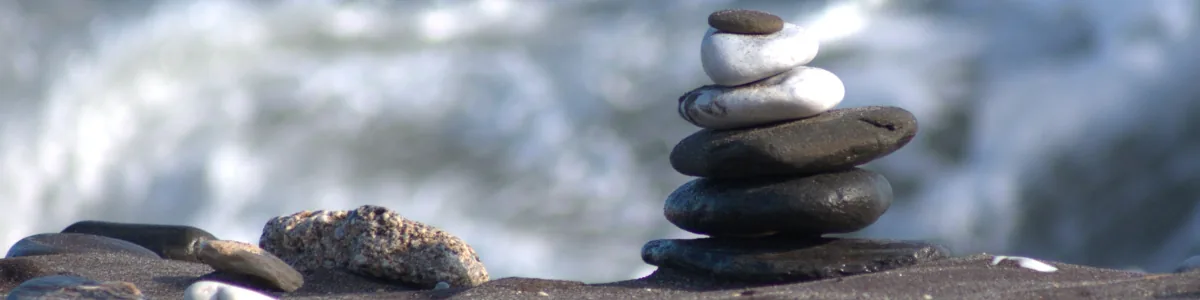 A stack of balanced pebbles on a beach, with the sea blurred behind