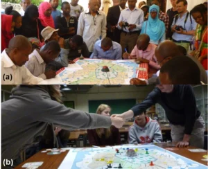(a) Game session organized with citizens in Moroni (Comoros Islands). (b) Interaction among Belgian students to develop a resilient community. Taken from Mossoux, S., et al. (2016)