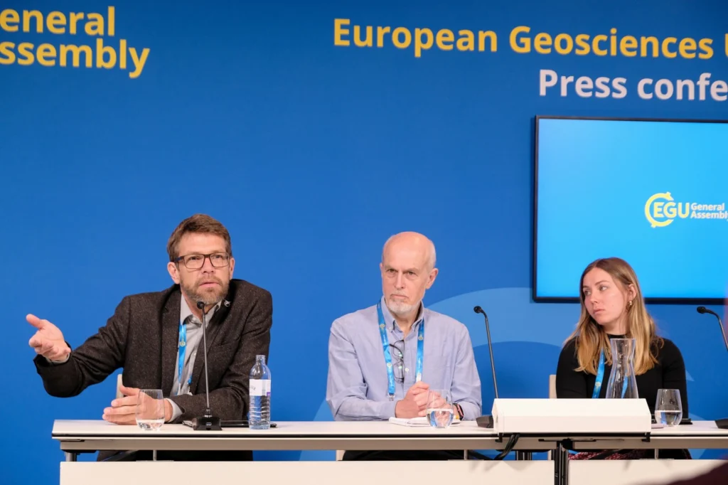 In front of the blue EGU press conference background, Olaf Eisen (left), Robert Larter (middle) and Emma Pearce (right) are engaged in discussion.
