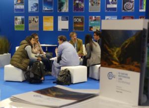 The image shows researchers networking and chatting about Science Policy at the EGU booth in 2023. 