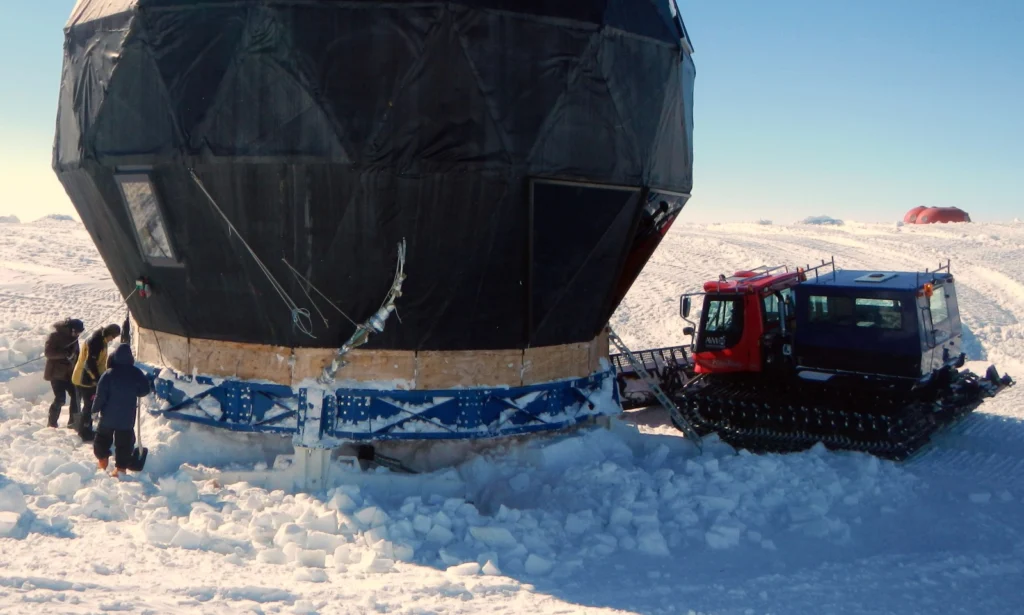 Freeing the dome using shovels, chainsaws and a pisten-bully. The skies are beginning to emerge from under the dome. The skis support the "bike wheel" (blue) that the dome is mounted on. 