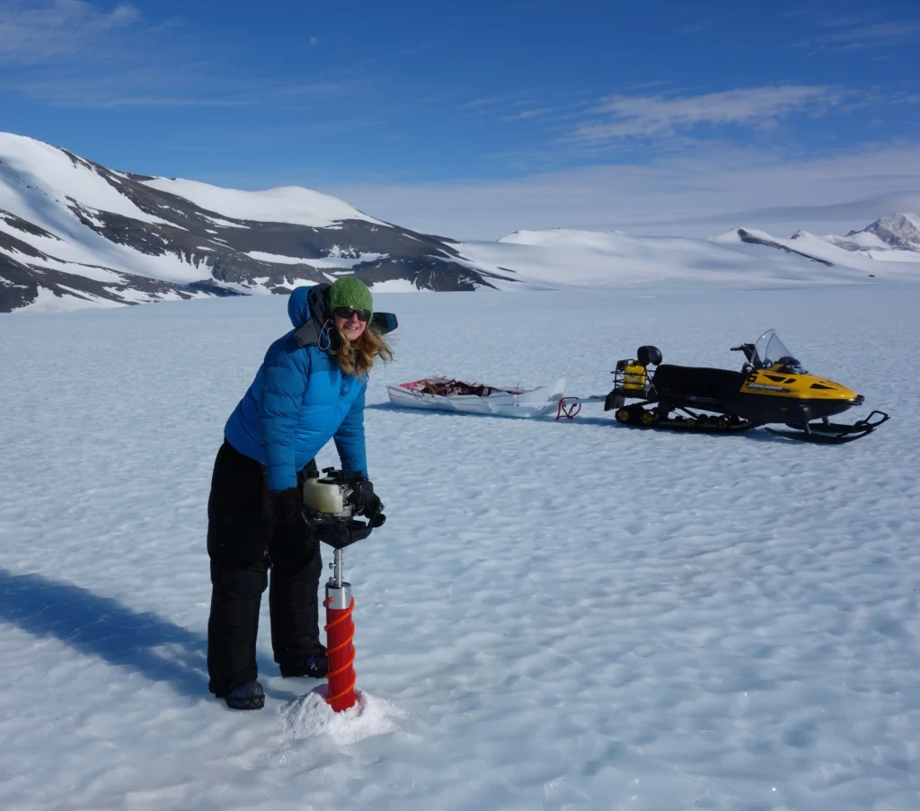 Drilling using a Kovacs corer. Here I'm wearing 3 coats: a light down jacket, a soft windproof shell, and my big down jacket on the top. I'm also wearing down trousers over my salopettes. It's quite windy on the blue ice, so it can feel very cold. (Credit: H. Millman)