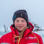 Imagine of person with red jacket and black AWI hat and snow in the background.