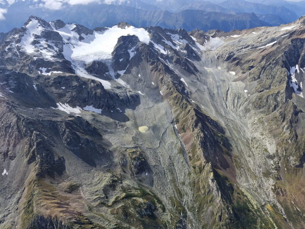Aerial image showing the climate change impact on small glaciers in the central Greater Caucasus, Georgia. Slopes are extensive deposits of moraines and loose rock debris, left behind by retreating glaciers. A small glacial lake (near the center-bottom of the image) fed by meltwater from the surrounding ice and snow was developed after glacier retreat [Credit: Levan Tielidze].
