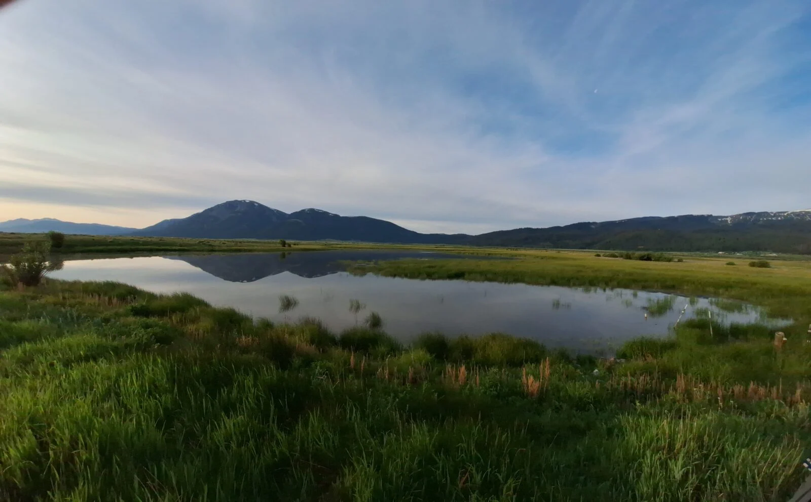 a scene scape with mountains in the background, a lake in the middle, and green grace in the foreground. 