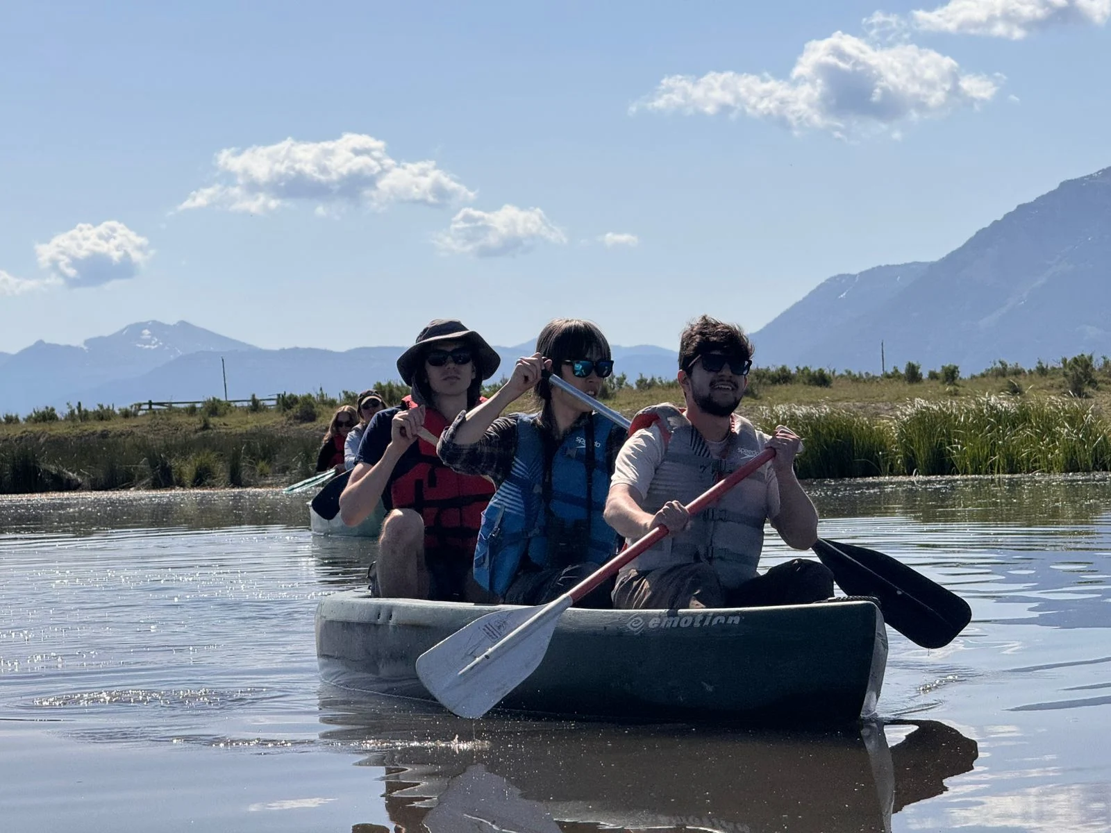 A group of three individuals in a canoe on a lake, with mountain in the distance. 