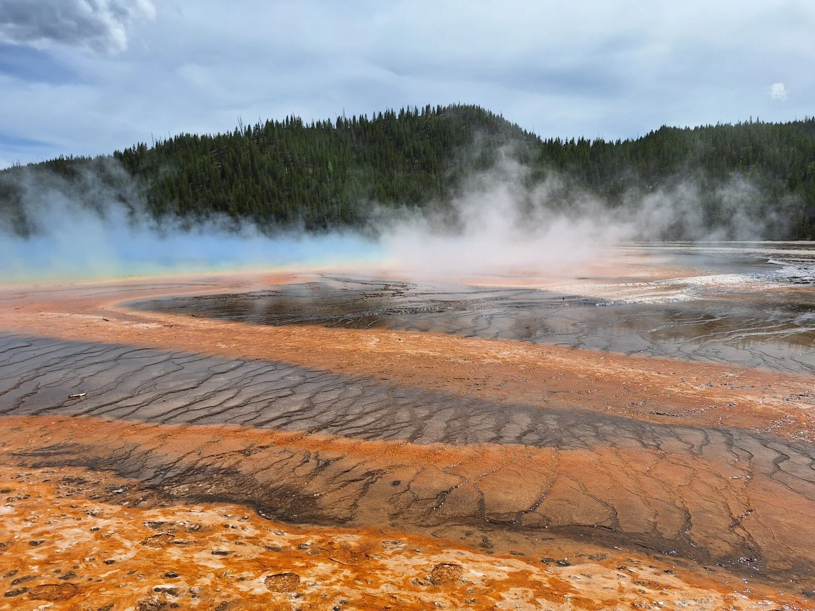 Spring water steaming with stripes of yellow and brown rock and sediment in front of the natural spring. 