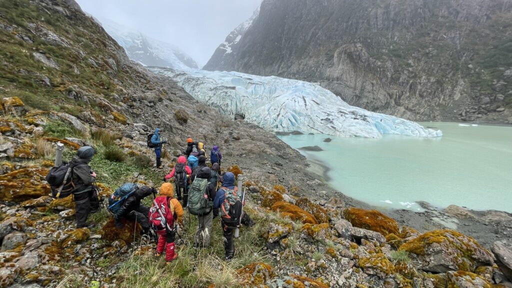 a group of students and staff in hi-vis rain gear pick theri way along a rocky slope towards a glacier