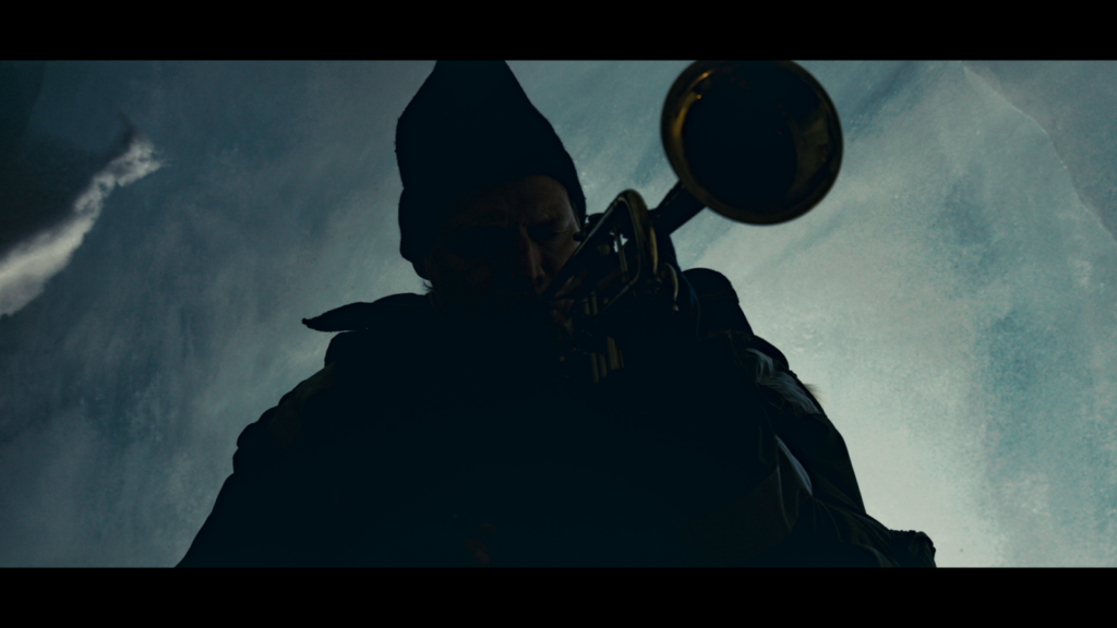 against a blue, muted sky a saxophone layer in a beanie plays a song
