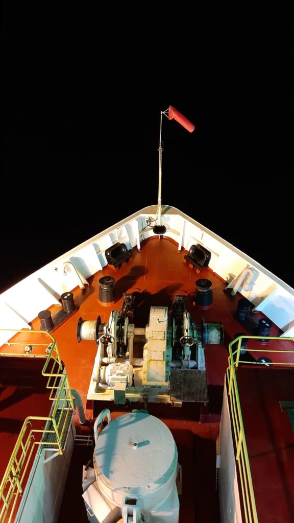 Photo at night looking down at the brightly lit front part of a ship with only dark night visible beyond