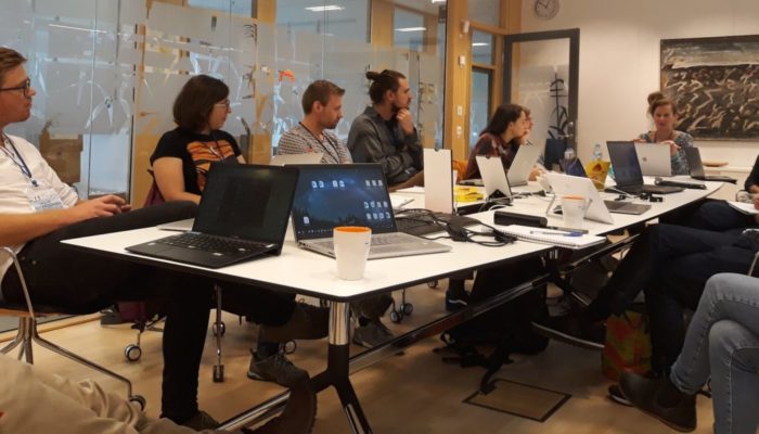 A group of people working together on laptops around a table in a room.