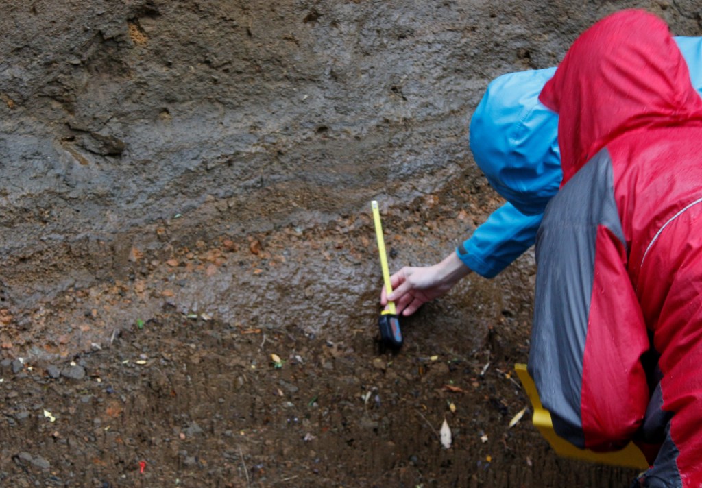 Karen Fontijn and Harriet Rawson measure up an ancient pumice deposit - the orange layer - in a road cut.  