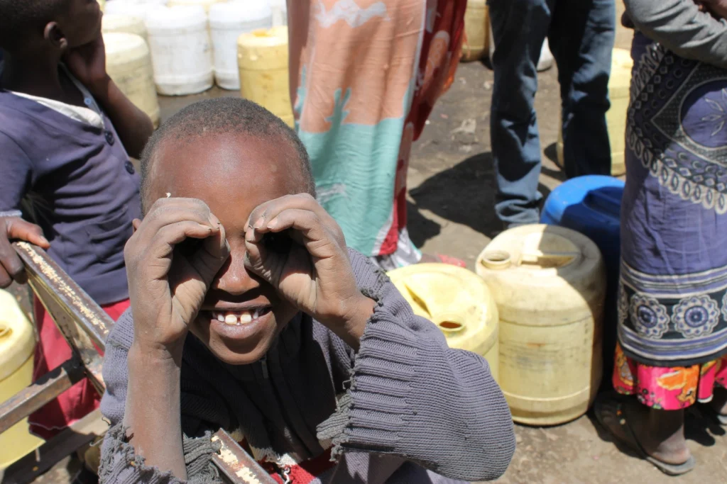 In this photo a kid of the Arusha region in Tanzania and several barrel of water. Part of Ines's current work deals with the environmental health issues in the area around Meru volcano in the Arusha region, Tanzania. People in this region are seriously affected by dental and skeletal fluorosis, which occurs as a consequence of drinking water containing levels of fluoride beyond acceptable limits for consumption (>1.5 mg/L). In addition, the respiratory health of inhabitants of areas around Meru, but also Oldoinyo Lengai volcano is potentially affected by volcanic dust re-mobilisation, especially during the dry season. Photo credit: Ines Tomašek.